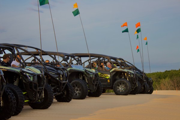 Row of off-road vehicles with flags parked on sandy terrain.
