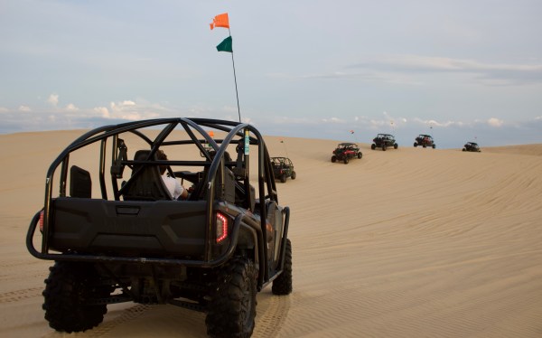Row of dune buggies driving on sand dunes under a cloudy sky.