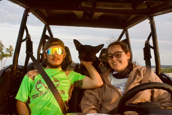 Two people and a dog in a vehicle, all smiling.