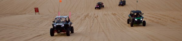 Four off-road vehicles driving on sandy dunes with visible tire tracks.