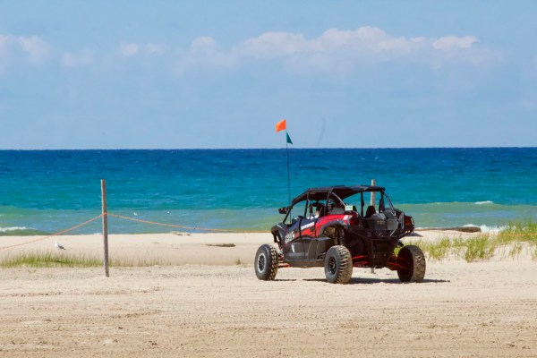 A dune buggy parked on a sandy beach near the ocean under a clear sky.