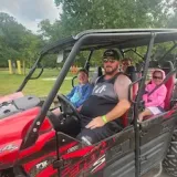 Man driving a red ATV with three passengers on a grassy area.