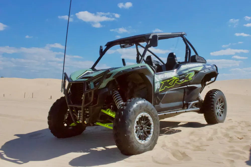 Off-road vehicle on sand dunes under a blue sky with clouds.